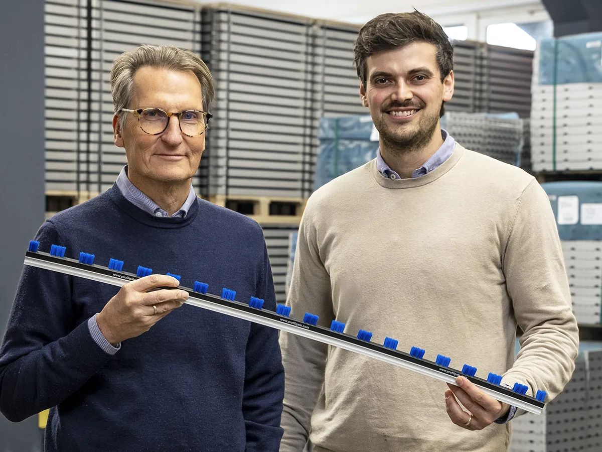 Christian und Cornelius Löwe stehen nebeneinander und halten ein ProfilGate® Bürstenleiste in der Hand.