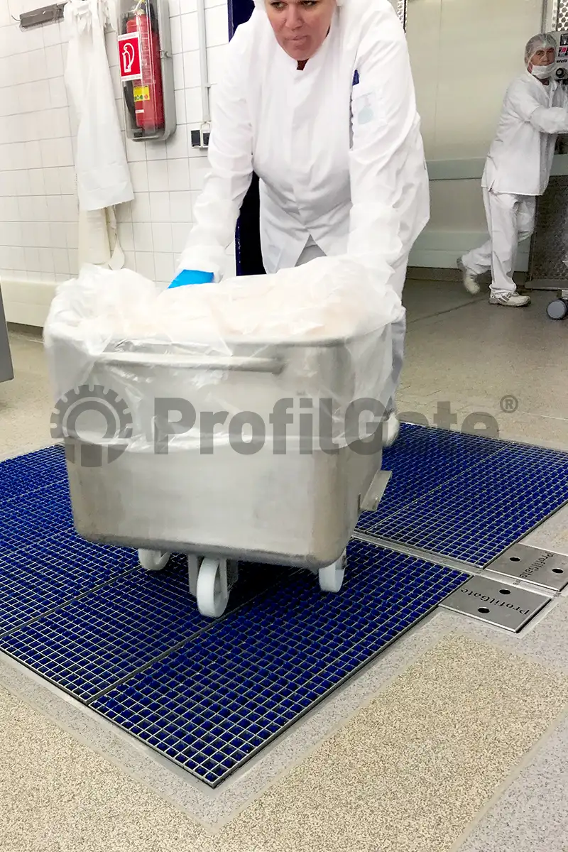 Mitarbeiter im Arbeitskittel schiebt Kutterwagen mit Lebensmittelwaren über eine Hygieneschleuse