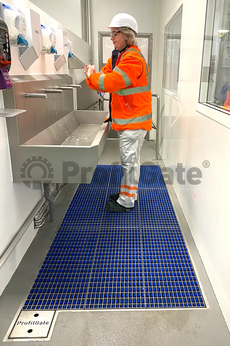Mitarbeiter in Arbeitskleidung steht auf einer Hygieneschleuse und wäscht sich die Hände an einem Waschbecken