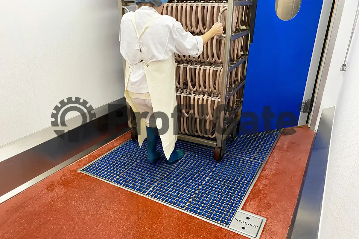 Person in weißem Arbeitskittel zieht Regalwagen mit Wurstwaren über eine Hygieneschleuse