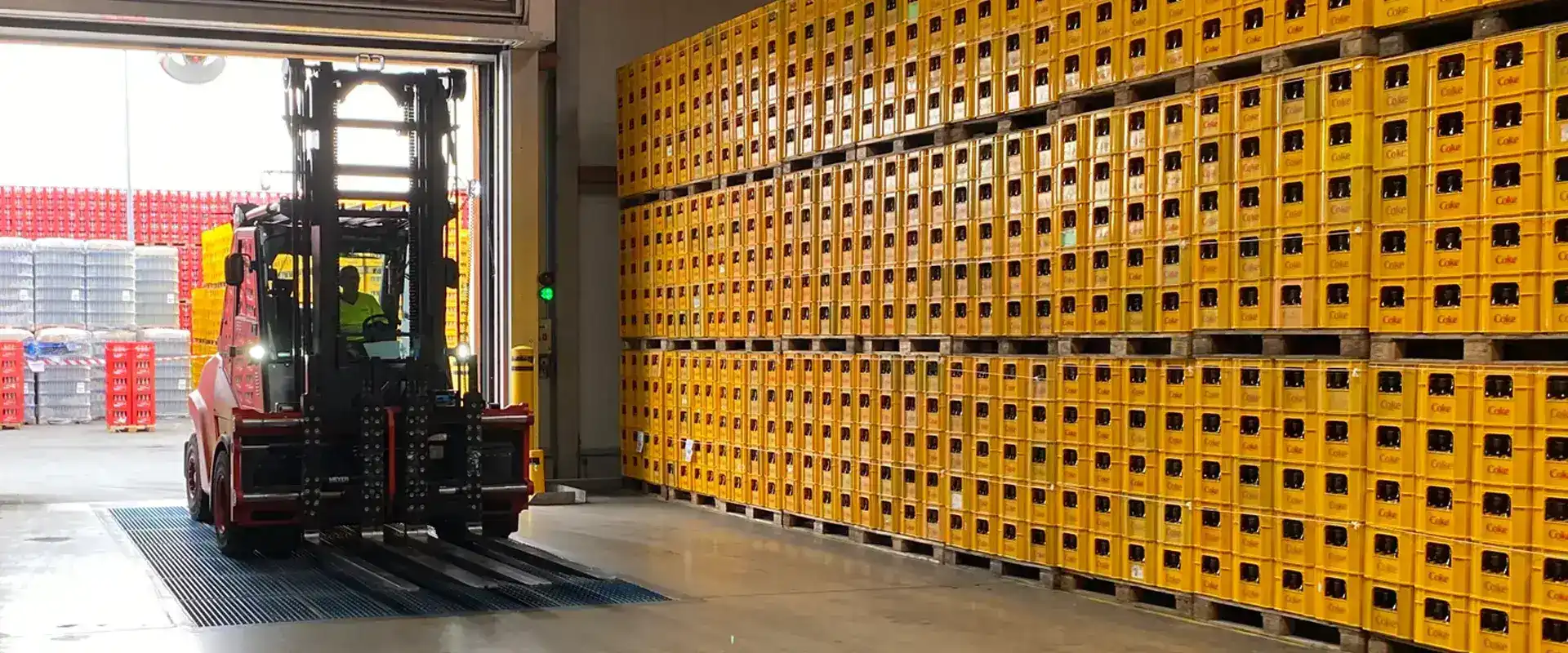 Ein Gabelstapler fährt über eine blaue Sauberlaufzone in die Logistik, am Rand stehen viele Coca-Cola Getränkekästen