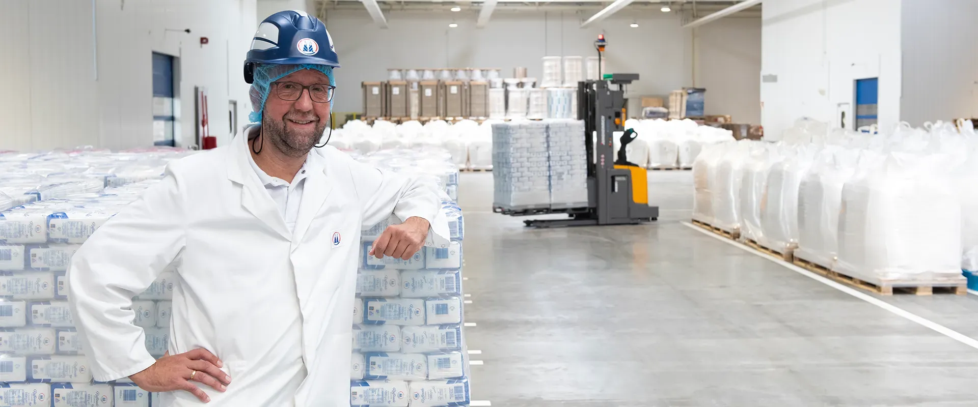 Ein Mitarbeiter aus dem Dispositionszentrum von Pfeifer und Langen steht in einer Logistikhalle, angelehnt an Industriesäcke